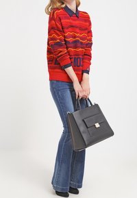 Červený svetr s vícebarevnými vzory, doplněný světle modrými rozšířenými džíny a černou koženou kabelkou s přední kapsou a stříbrnou sponou.