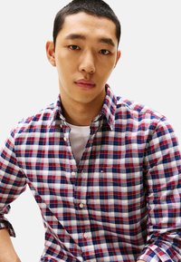 Camisa de cuadros en rojo y azul marino de tela ligera, con cuello clásico y mangas largas con puños abotonados.