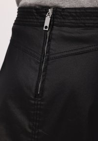 Schwarzer Rock mit verdecktem Reißverschluss an der Taille, strukturiertem Stoff und mit Zierstichen entlang der Nähte veredelt.