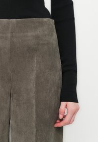 Gray corduroy pants with vertical ribs, paired with a black long-sleeve top. The fabric has a soft texture and a high-waisted design.