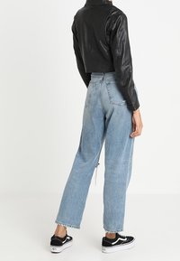 Veste en cuir noir courte avec un col haut, associée à un jean en denim bleu clair taille haute avec une coupe décontractée et des ourlets effilochés. Baskets noires.