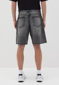 Pantalones cortos de mezclilla gris oscuro con un dobladillo deshilachado, bolsillos traseros y una cintura elástica, combinados con calcetas blancas y zapatillas grises.