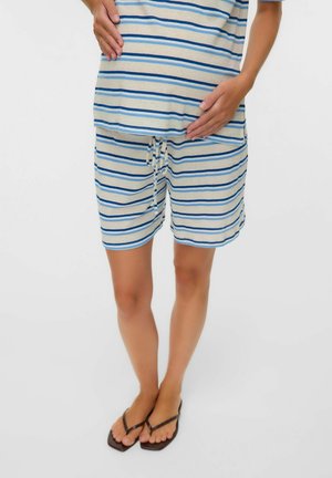 Personne portant un pyjama rayé bleu et blanc, debout pieds nus avec les mains reposant doucement sur un ventre arrondi.