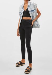 Chaleco de mezclilla con bordes sin rematar, top corto negro, jeans ajustados negros y sandalias de plataforma negras con detalles de hebilla.