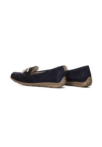 Marineblauwe suede instappers met beige rubberen zolen, voorzien van een decoratieve metalen accent aan de voorkant en een ronde vorm voor comfort.