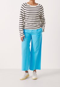 Gestreepte trui in crème en marineblauw, gecombineerd met wijde, effen turkooise broek en witte sneakers, met een relaxed fit en casual stijl.