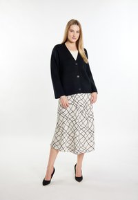 Schwarze Strickjacke mit V-Ausschnitt, ausgestattet mit drei Knöpfen. Kombiniert mit einem cremefarbenen Rock, der mit einem schwarzen Karomuster und silbernen Akzenten verziert ist.