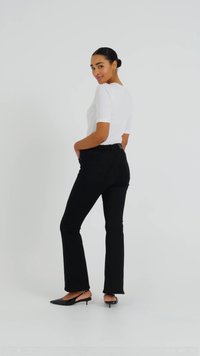 Top bianco a maniche corte, pantaloni neri aderenti e scarpe col tacco nere. L'outfit presenta una vestibilità comoda con una texture di tessuto liscia.