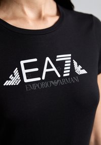 Svart bomull T-skjorte med en hvit grafisk logo "EA7 Emporio Armani," med stripete detaljer og små stjerner.