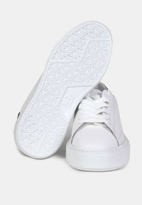 Baskets blanches avec tige en cuir lisse, lacets blancs et semelle en caoutchouc texturée, arborant un design minimaliste et des accents de talon contrastants.