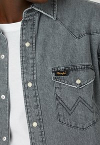 Šedá denimová košile s špičatým límcem, patentními knoflíky a náprsní kapsou se šitým zigzag vzorem a logem Wrangler.