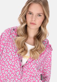 Różowa kurtka z jasnoniebieskim wzorem w panterkę, wyposażona w przedni zamek błyskawiczny, zatrzaski oraz miękką, gładką fakturę. Noszona na białej koszuli.