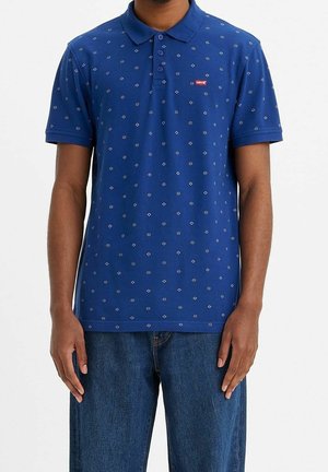 Marineblaues Poloshirt mit einem bestickten Muster aus kleinen Rauten und Punkten, mit einer dreiknöpfigen Knopfleiste und einem Logetikett auf der Brust.