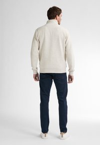 Beżowy sweter o fakturze z wysokim kołnierzem, w połączeniu z granatowymi spodniami i jasnym obuwiem. Neutralne kolory i prosty design.