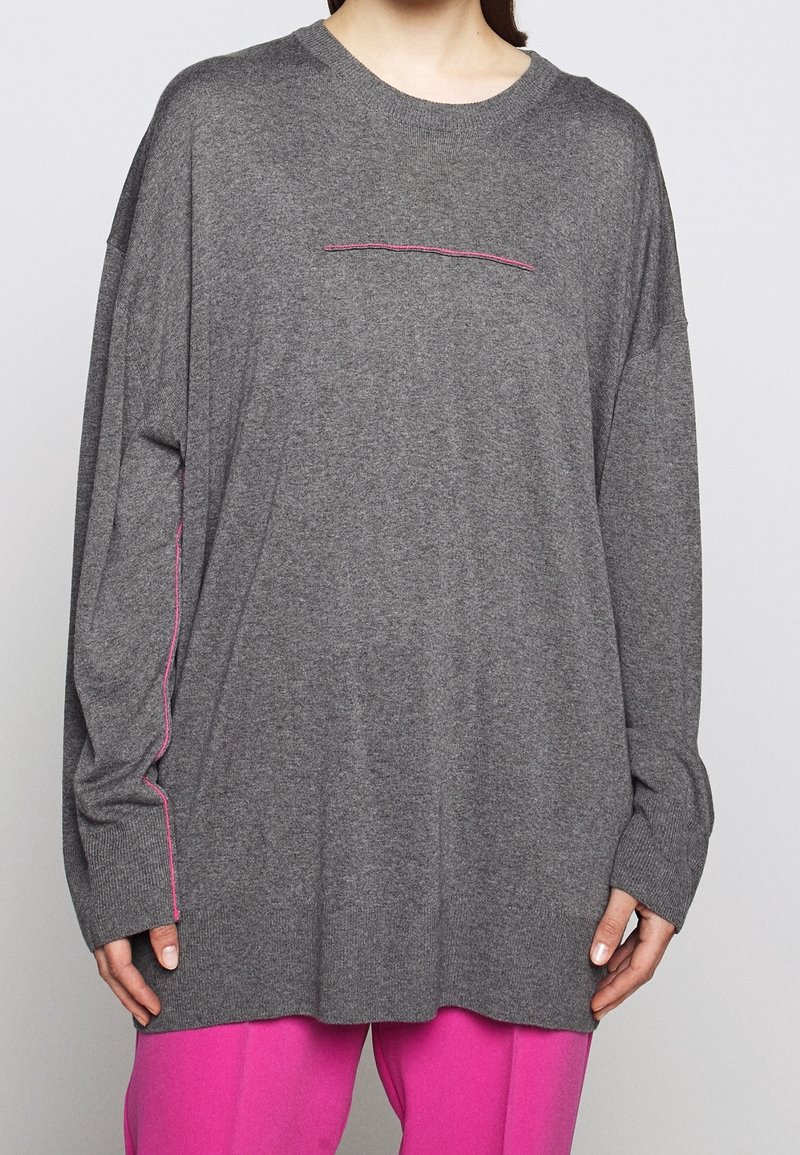 Gray oversized sweater with long sleeves, featuring a horizontal pink stitch detail across the chest and pink accents along the sleeves.