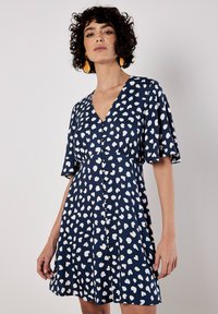 Navy Kleid mit weißen herzförmigen Mustern, V-Ausschnitt, Knopfverschluss und kurzen, schwingenden Ärmeln. Glattes Material und A-Linien-Schnitt.