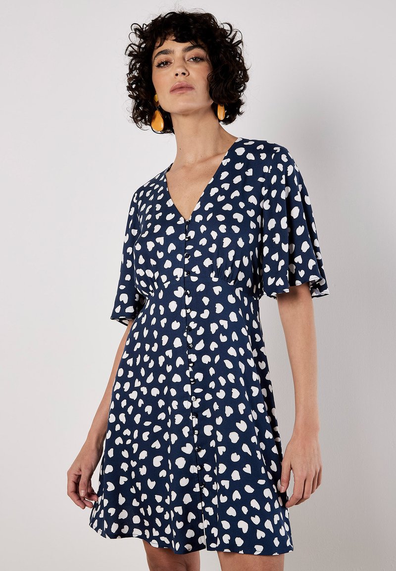 Navy Kleid mit weißen herzförmigen Mustern, V-Ausschnitt, Knopfverschluss und kurzen, schwingenden Ärmeln. Glattes Material und A-Linien-Schnitt.