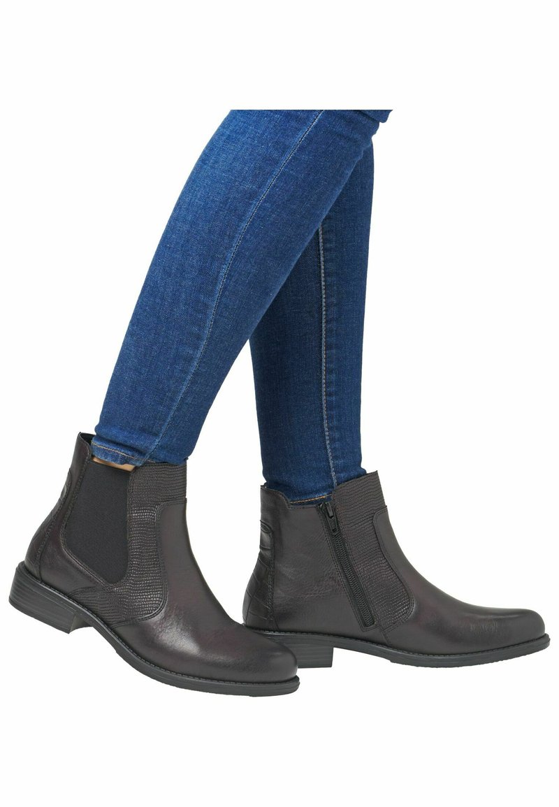 Czarne skórzane botki za kostkę z elastycznymi panelami bocznymi, smukły design, niski słupkowy obcas i teksturowane akcenty. Noszone z dopasowanymi niebieskimi dżinsami.