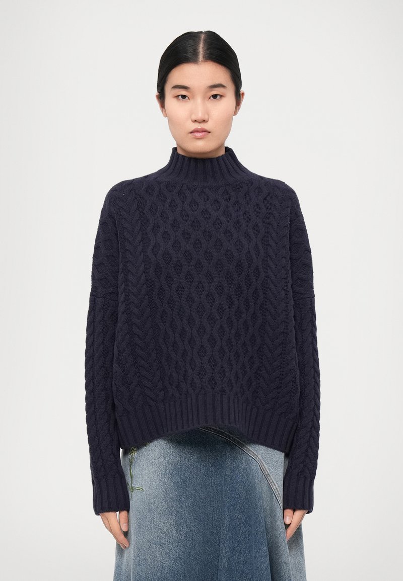 Navy blue knitted sweater with a high collar and textured cable pattern. Loose fit with ribbed hems and long sleeves.