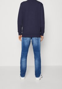 Navy sweatshirt with ribbed cuffs, paired with light blue faded jeans. White sneakers complete the casual outfit.