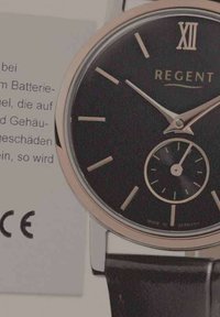 Montre analogique noire avec un boîtier en rose gold poli, présentant un cadran minimaliste, de fines indices horaires, un petit sous-cadran et un bracelet en cuir.