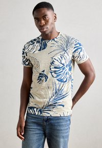 Krátky béžový tričko s modrou tropickou potlačou, so soft dotykom a okrúhlym výstrihom, doplnené modrými džínsami.