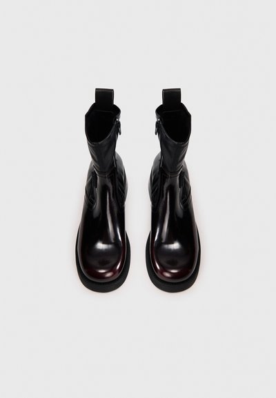 Μαύρα δερμάτινα μποτάκια αστραγάλου με γυαλιστερό φινίρισμα, στρογγυλεμένες μύτες, φερμουάρ στο πλάι και θηλιές στο πάνω μέρος για εύκολη φορεσιά.