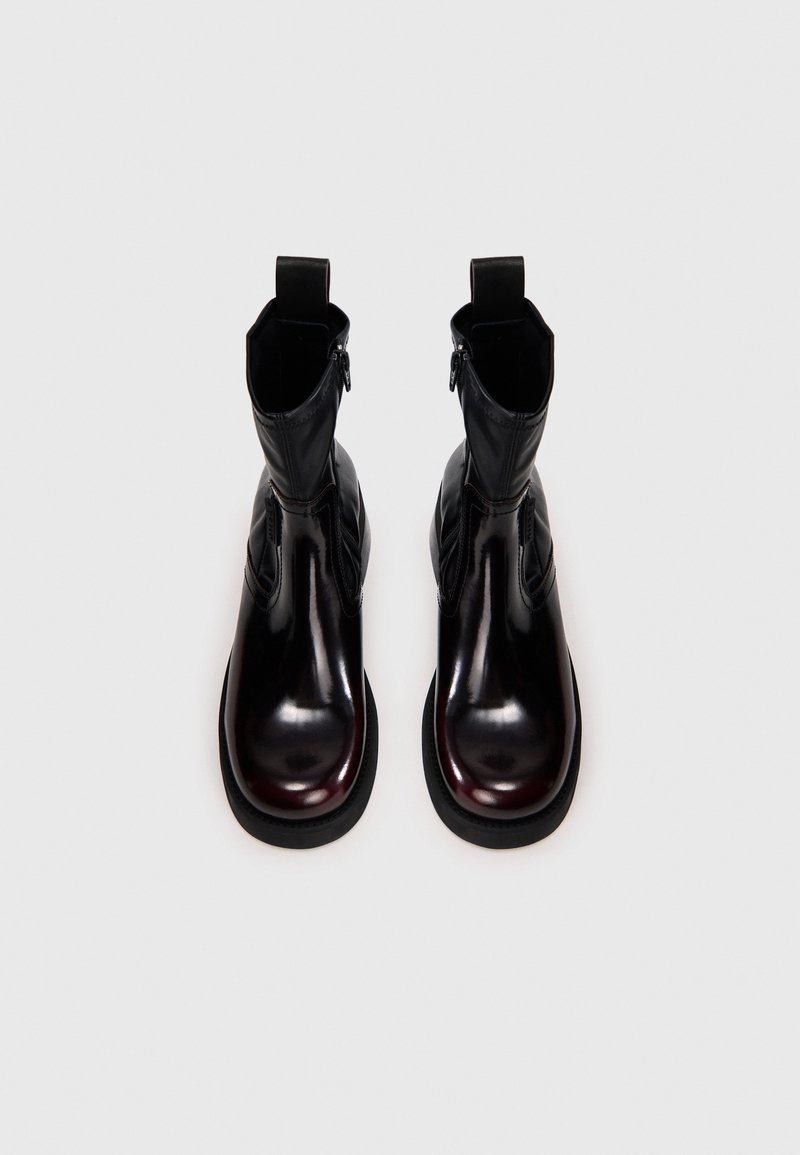 Sorte læderankelstøvler med en blank finish, runde tæer, en sidelukning med lynlås og trækflapper øverst for nem påtagning.