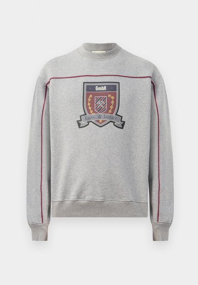 Felpa grigia con collo rotondo a coste, che presenta una grafica centrale a forma di scudo nei colori rosso, blu e oro, con il testo "Amore & Giustizia" e cuciture decorative.