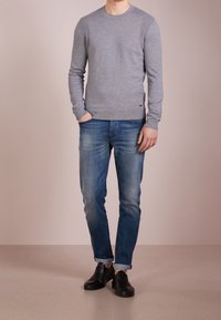 Grauer Strickpullover mit Rundhalsausschnitt, gerippten Akzenten, kombiniert mit blauen Denim-Jeans und schwarzen Sneakers. Einfaches, lässiges Outfit.