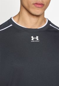 Μαύρο αθλητικό μπλουζάκι με κοντά μανίκια, κατασκευασμένο από λείο ύφασμα, με αντιθετικές λευκές λεπτομέρειες στο γιακά και τους ώμους.