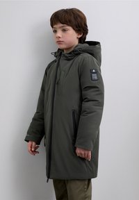Groene, geïsoleerde parka met capuchon, voorzien van een ritssluiting aan de voorkant en zijzakken. Heeft een badge op de mouw en een glad, strak oppervlak.