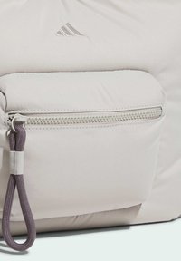 Light gray backpack with a textured surface, featuring a front zip pocket and a gray loop pull for easy access. бренда Adidas logo on top.