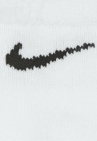 Calzino bianco in cotone con un grande logo swoosh nero della Nike. Motivo a maglia testurizzato con bordo rigato. Design minimalista.
