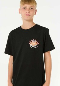 T-shirt en coton noir avec un petit logo de surf multicolore et des rayons de soleil stylisés sur la poitrine gauche. Manches courtes, col rond.