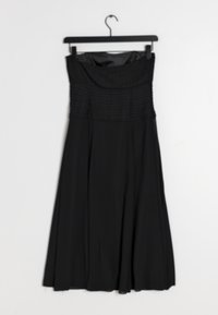 Černé bezramínkové šaty s plisovanou korzetovou částí a splývavou sukní visí na černém ramínku na bílém pozadí. Hladká textura.