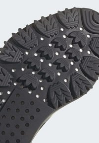Black rubber shoe sole with a textured pattern featuring leaf-like shapes, raised ridges, and perforated sections for grip and flexibility.
