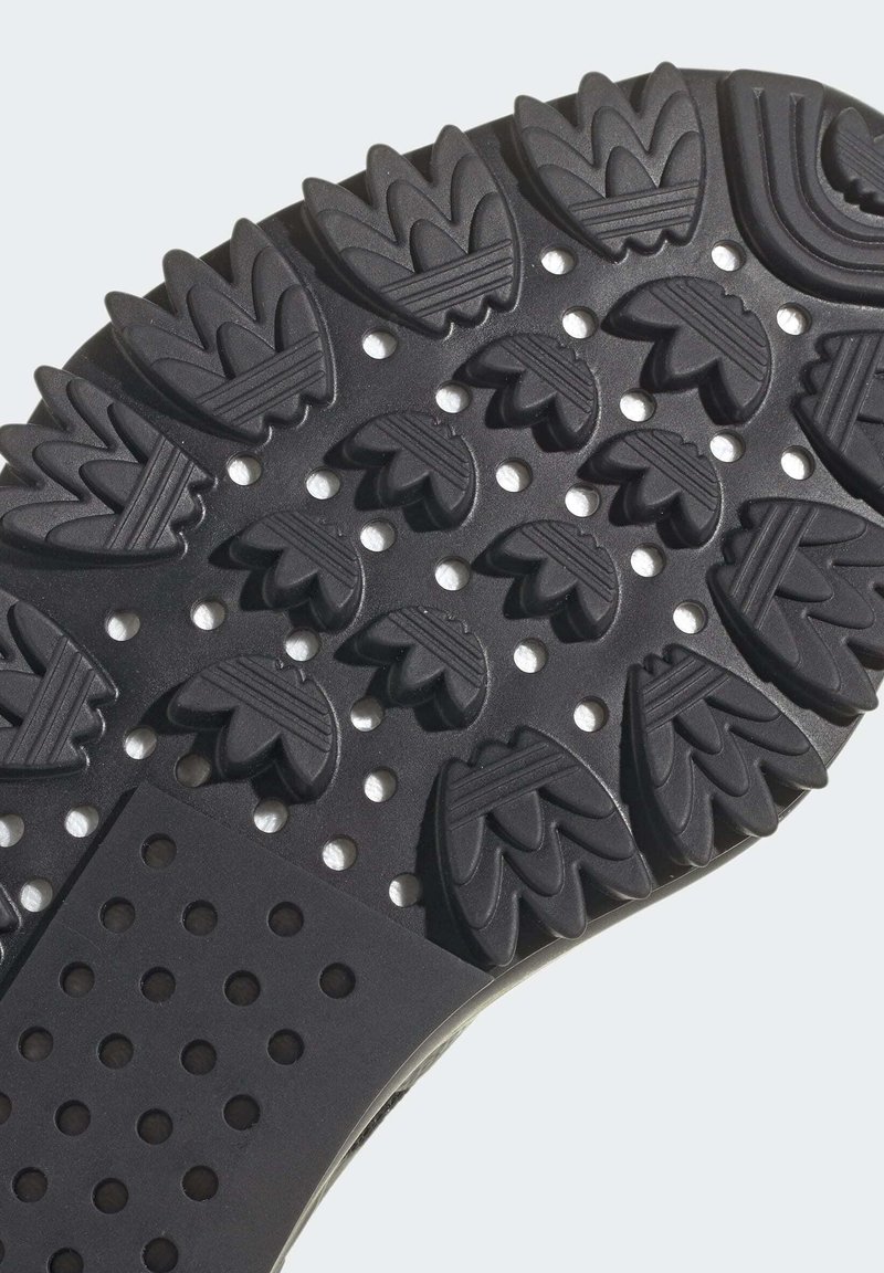 Suela de zapato de goma negra con un patrón texturizado que presenta formas similares a hojas, crestas elevadas y secciones perforadas para mayor agarre y flexibilidad.