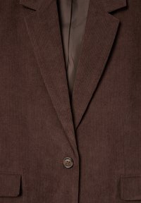 Brązowa marynarka z korduroyu w pionowe paski, z pojedynczym zapięciem na guzik i dwoma przednimi kieszeniami. Podszewka z ciemniejszego brązowego materiału.