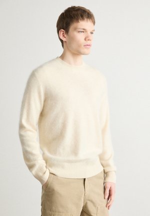 Maglione color crema realizzato in tessuto morbido. Presenta un colletto rotondo e polsini e orlo ribattuti. Abbinato a pantaloni cargo beige.