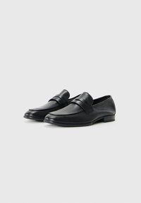 Mocasines de cuero negro con punta redondeada, que presentan dos correas horizontales a lo largo del empeine y un tacón bajo. Textura suave y diseño elegante.