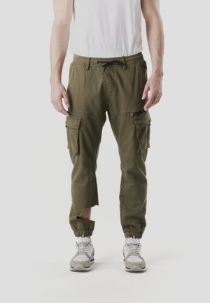 Pantalones cargo verdes oliva con múltiples bolsillos, puños elásticos y cintura con cordón ajustable. Presentan un corte en el tobillo izquierdo.