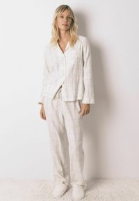 Hvid pyjamas sæt med et rutenet mønster, lavet af blødt stof. Består af en knap-op skjorte og bukser med snor i livet, komplet med hyggelige slippers.