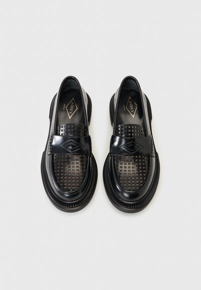 Μαύρα δερμάτινα μοκασίνια με τετράγωνες διάτρητες τρύπες, χοντρές σόλες και διαμαντένια λεπτομέρεια στο λουράκι, παρουσιάζονται από πάνω σε λευκό φόντο.