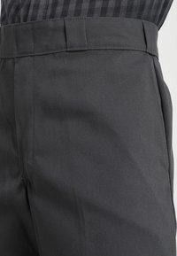 Mörkgrå skräddarsydda byxor med bälteshål som bärs med en instoppad svart och grå rutig skjorta.