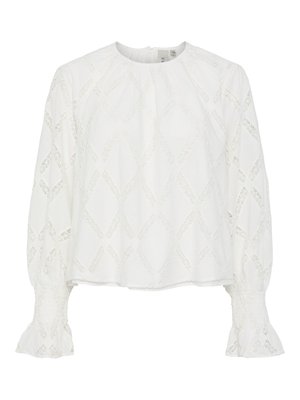 Blouse blanche avec un motif de diamant texturé et des manches bouffantes avec des poignets smockés. Encolure ronde ; tissu léger et respirant.