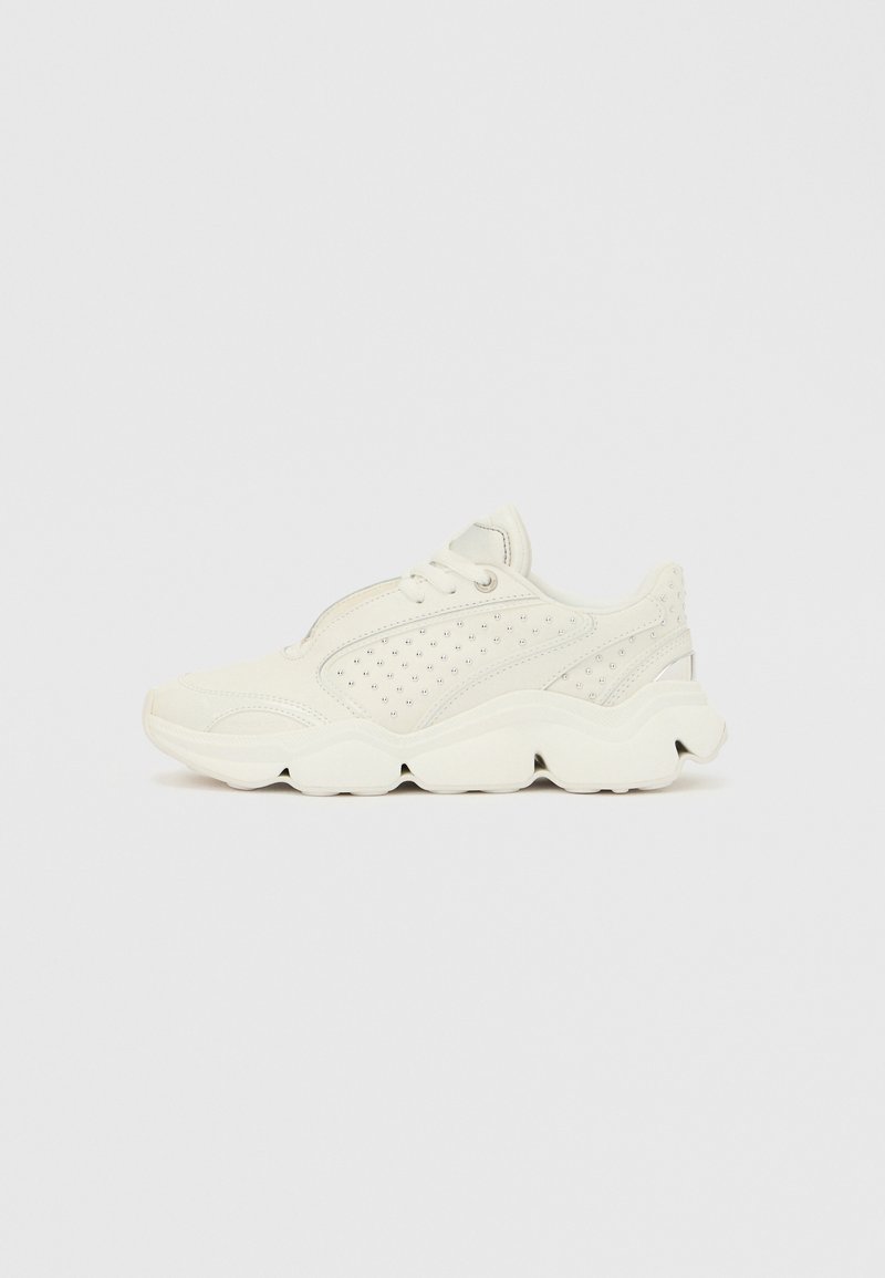 Balts sneakeris ar teksturētu augšdaļu, kas izceļas ar caurumiem, auklu aizdari un biezām, viļņainām zolēm, kas nodrošina amortizāciju.