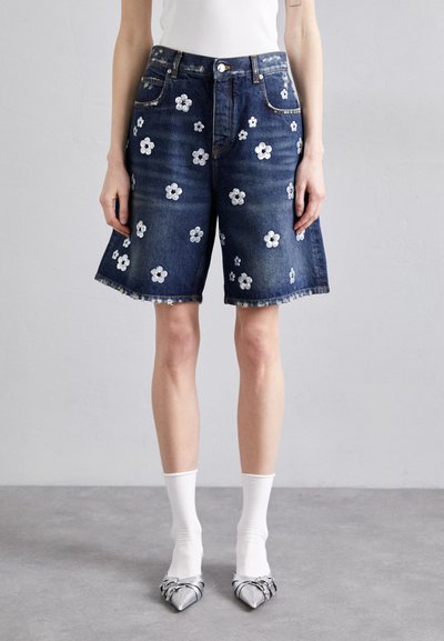 Shorts di denim con lavaggio scuro, caratterizzati da ricami floreali bianchi, bordi grezzi e cinque tasche, abbinati a calze bianche e tacchi d'argento.