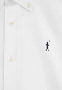 Witte overhemd met knopen en een klein zwart geborduurd logo van een persoon die een hamer draagt op het linkerborstgebied.