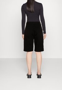 Mustat farkkubermudat puolivälissä reittä, suora leikkaus, viisi taskua ja sileä pinta. Yhdistetty pitkähihnaiseen toppiin.